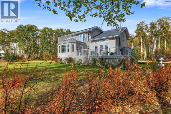 Backyard view of a light gray house with a large deck, a sunroom, and surrounding autumnal foliage. - 94038b -- 702 Township, Rural Grande Prairie No  1, County Of