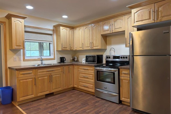 Corner kitchen with light oak cabinets, stainless steel appliances, and a double sink. - 94067 Wilson Road, Shoal Lake