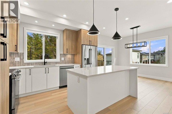 Kitchen with a large island, white countertops, light wood cabinets, and stainless steel appliances with pendant lights. - 941 Malbec Link, Langford