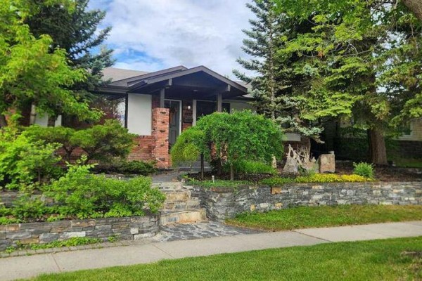 Close-up of the front entrance of the house with stone landscaping and trees. - 9415 Fairmount Drive Se, Calgary