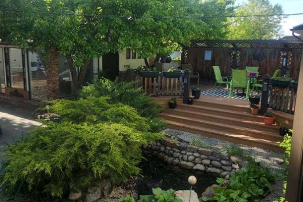 Wooden deck with green chairs and tables overlooking a garden with a small pond. - 9415 Fairmount Drive Se, Calgary