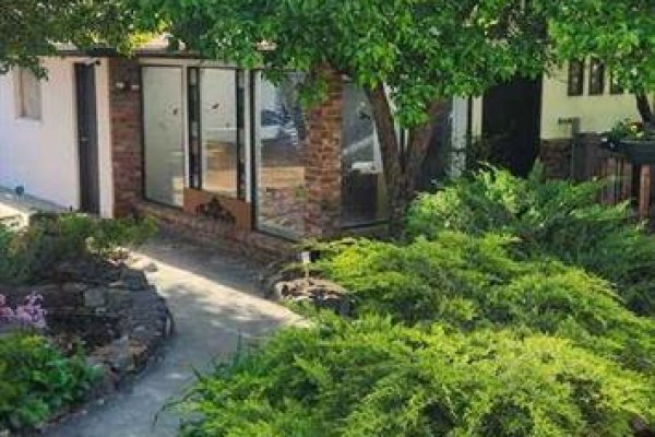 View of the house exterior with large windows, brick accents, and lush green bushes. - 9415 Fairmount Drive Se, Calgary