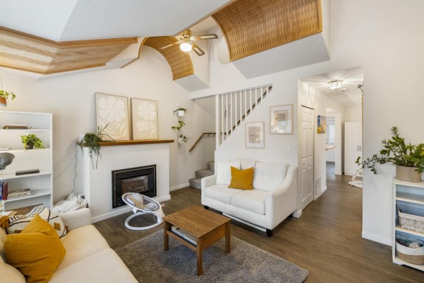Living room interior showing white sofas, fireplace, vaulted ceiling with wood accents, and staircase. - 9418 Mcnaught Road, Chilliwack Proper East, Chilliwack