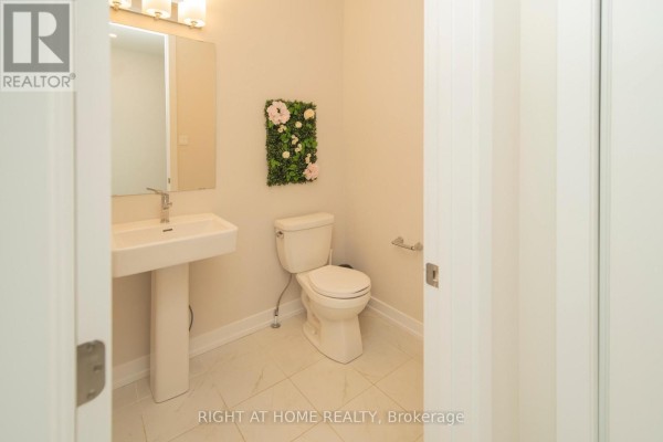 Powder room with a white pedestal sink, toilet, and tiled floor with floral wall decor. - 942 Seagrave Lane, Ottawa