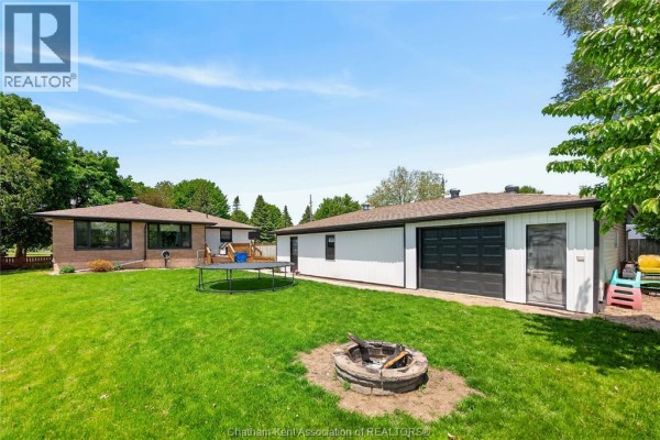 View of the backyard showing the house, garage, trampoline, and fire pit. - 944 Mcnaughton Avenue, Chatham