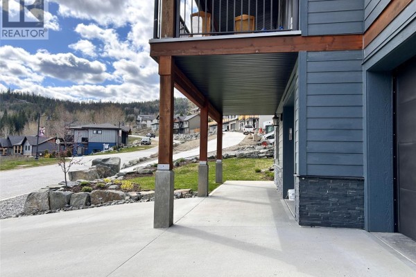 Concrete walkway under a covered balcony, leading past garage doors of a grey house. - 944 Redstone Drive, Rossland