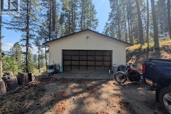 A detached two-car garage with a glass-paned overhead door sits on a concrete pad. - 9456 Houghton Road, Vernon
