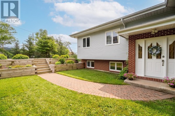 Side view of a two-story house with red brick and grey siding exterior, surrounded by green lawn. - 946 Indian Meal Line, Portugal Cove   St  Phillips