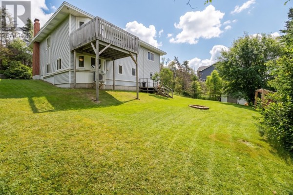 Rear exterior of the house featuring a wooden deck, green lawn, and mature trees. - 946 Indian Meal Line, Portugal Cove   St  Phillips