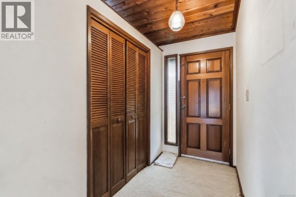 Interior entryway with a wooden door, beige carpet, and a large louvered closet. - 946 Paconla Pl, Central Saanich
