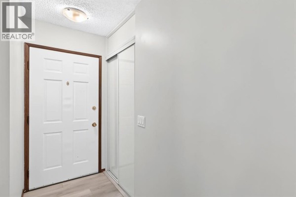 Interior entryway with a white door, wood trim, and a mirrored closet door. - 947 Maitland Way Ne, Calgary