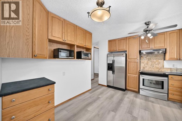 Kitchen with oak cabinetry, stainless steel appliances, and a view down a hallway. - 947 Maitland Way Ne, Calgary
