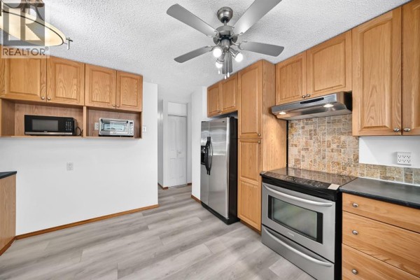 View of the kitchen featuring oak cabinets, stainless steel refrigerator, and ceiling fan. - 947 Maitland Way Ne, Calgary