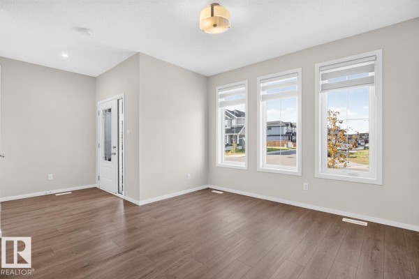 Living room with three large windows, grey walls, and dark wood-look flooring. - 9478 Colak Ln Sw Sw, Edmonton