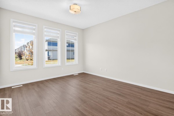 Empty room with three windows, grey walls, and dark wood-look flooring. - 9478 Colak Ln Sw Sw, Edmonton