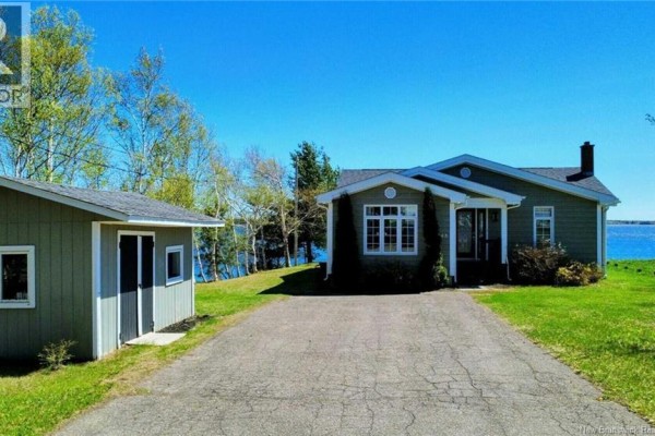 Exterior of a light green house with a detached garage and driveway, water in the background. - 948 Rue Des Chalets Street, Tracadie