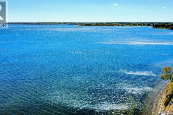 Expansive view of a wide, blue lake under a clear sky with a grassy shoreline. - 948 Rue Des Chalets Street, Tracadie
