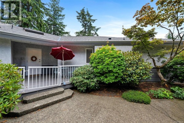 A covered porch with a red umbrella and white railing outside the entrance of a grey house. - 949 Pacific Pl, Duncan