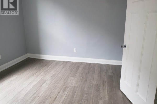 Empty room with light grey walls, grey wood-look laminate flooring, and a doorway with a black mat. - 95 Cayuga Street Unit# 2, Brantford