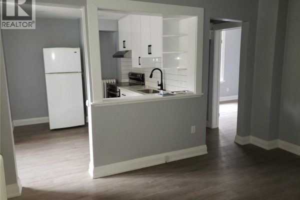 Empty room with light grey walls, grey wood-look laminate flooring, and an open white door. - 95 Cayuga Street Unit# 2, Brantford