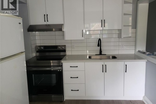 View into a kitchen with white cabinets and a small breakfast bar, next to a living area. - 95 Cayuga Street Unit# 2, Brantford
