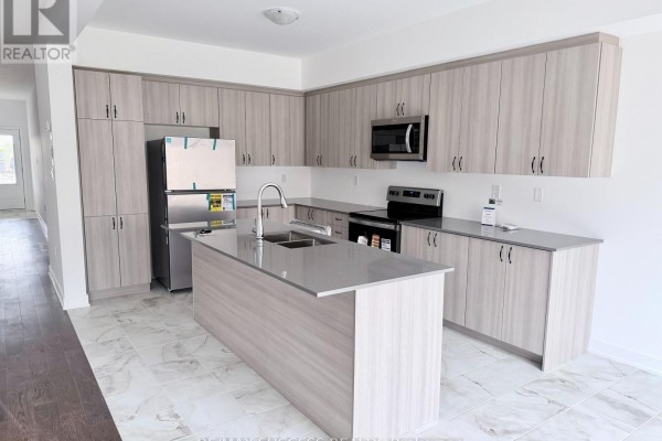 Modern kitchen with light wood cabinets, stainless steel appliances, a grey island, and tile flooring. - 95 Flan Boulevard, Barrie