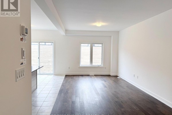 Empty living room with dark hardwood floors, white walls, and a large window overlooking a yard. - 95 Flan Boulevard, Barrie