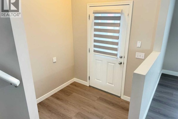 View of the entryway from the top of the stairs, showing a white door with blinds, wood-look flooring, and light grey walls. - 95 Panora Close Nw, Calgary