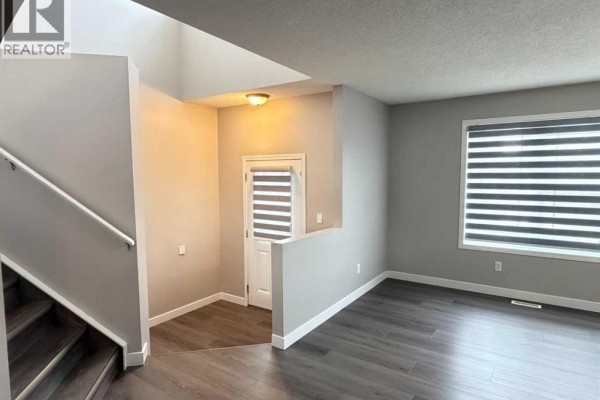 Living room area adjacent to the entryway, featuring dark wood-look flooring, a large window with blinds, and neutral wall colors. - 95 Panora Close Nw, Calgary