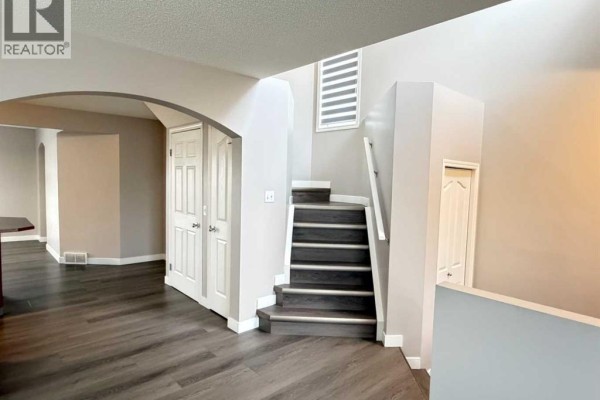 Interior staircase with dark treads and grey risers, leading past a grey archway with double doors and into the main living space. - 95 Panora Close Nw, Calgary