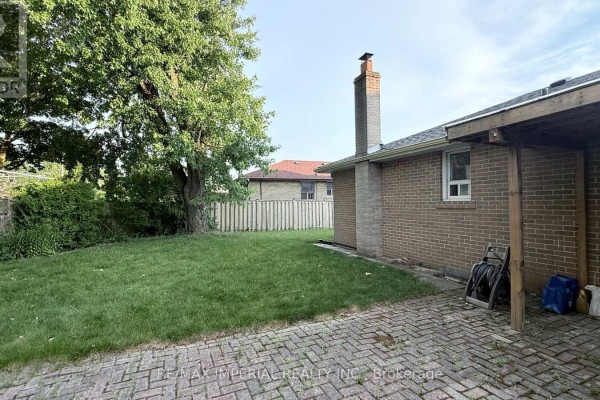 Backyard with a brick patio, grass lawn, wooden fence, and brick chimney. - 95 Pleasant View Drive, Toronto