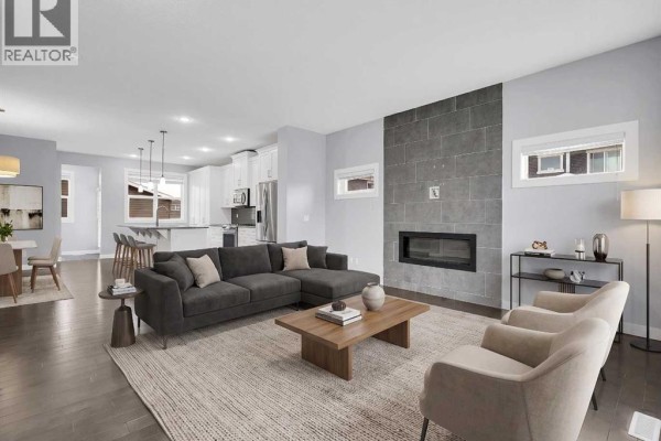 Living room with a sectional sofa, fireplace with stone surround, and open-concept kitchen view. - 95 Redstone Park Ne, Calgary