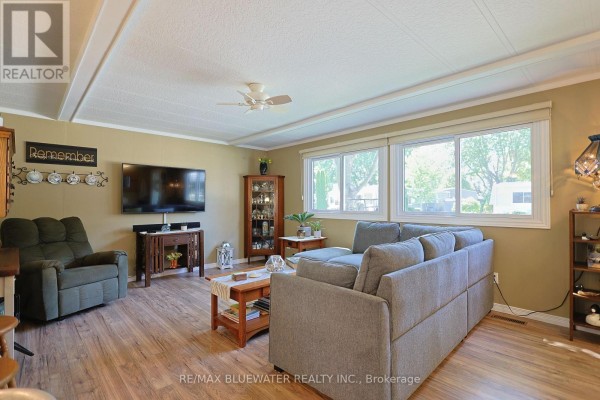 Living room with a grey sofa, recliner, wood-look flooring, and large windows. - 95 Shannon Boulevard, South Huron