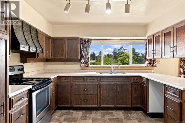 Kitchen with dark wood cabinets, stainless steel stove, and a window overlooking trees. - 950 Dunn Ave, Saanich
