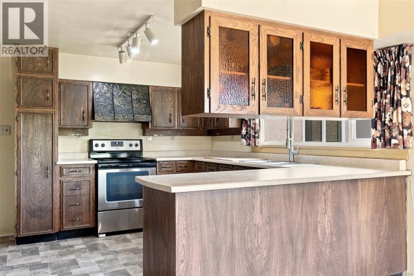 Kitchen island with dark wood base and a lighter countertop, facing the sink. - 950 Dunn Ave, Saanich