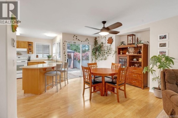 Open-concept dining area and kitchen with light wood cabinets, a round table, and sliding glass doors. - 950 Mcdonald St, Duncan