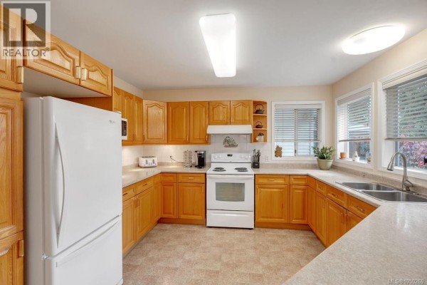 Spacious kitchen with light oak cabinets, white appliances, and a double sink overlooking the garden. - 950 Mcdonald St, Duncan