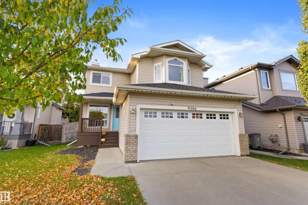 Front exterior of a beige house with a blue front door and green lawn. - 9506 83 Av, Morinville