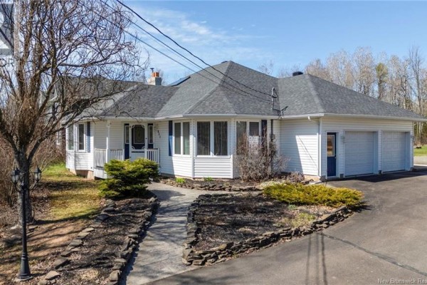 Side view of a white bungalow with a grey roof, a paved driveway, and a separate white garage. - 951 Ryan Street, Moncton