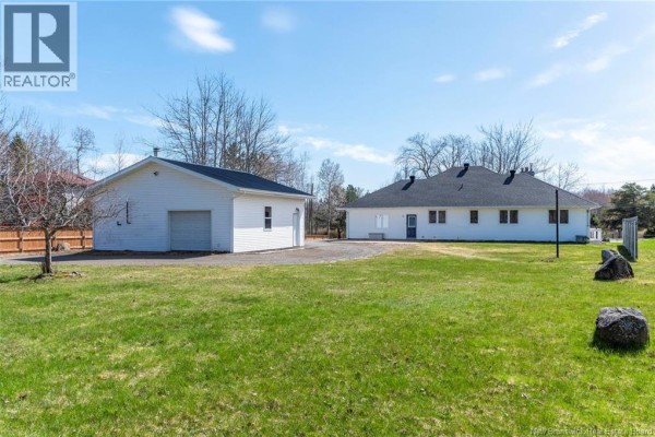 Rear view of the white bungalow and the detached white garage with a grassy yard. - 951 Ryan Street, Moncton