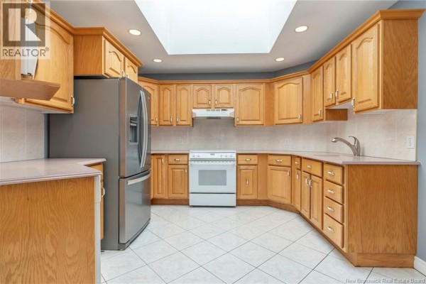Kitchen showing wood cabinets, stainless steel refrigerator, white stove, tiled floor, and skylight. - 951 Ryan Street, Moncton