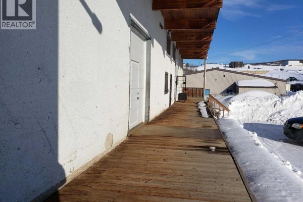 Wooden boardwalk along commercial building exterior with snow piles and a dark car. - 9510 90 Avenue, Peace River
