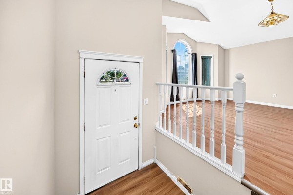 Interior view of the entryway, showing a white front door, wood floors, and staircase with white railing. - 9518 106 Av Nw, Edmonton