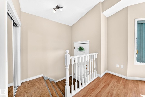 Interior view of the entryway showing a white door, staircase, wood floors, and beige walls. - 9518 106 Av Nw, Edmonton