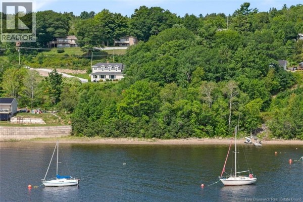 Distant view of houses on a wooded hill overlooking a bay with two sailboats moored. - 9531 Route 102, Morrisdale