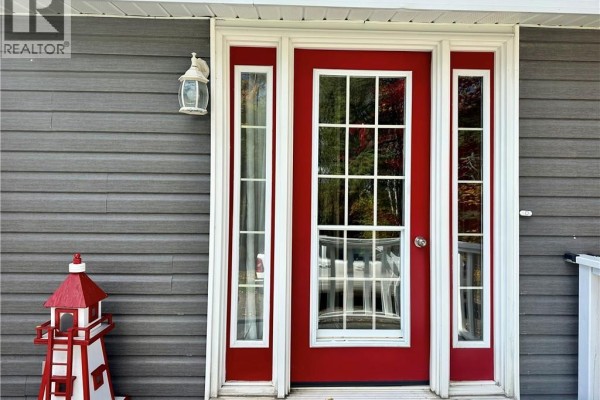 Red front door with glass panes and sidelights, set in grey siding. - 954 Main Street, Grand Sault/grand Falls