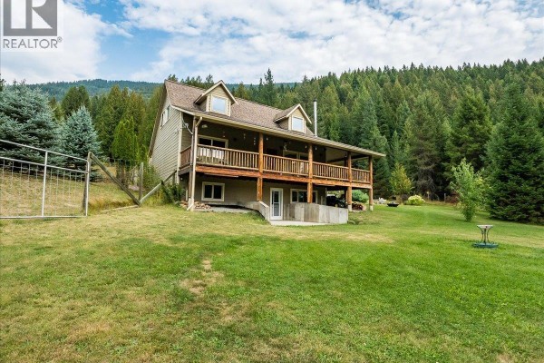 Covered wooden deck wraps around the side of the house with outdoor furniture visible. - 955 Cedar Brae Road, Glade
