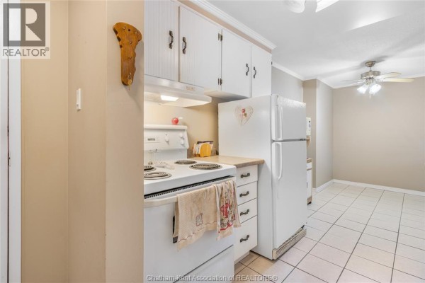 Kitchen view showing white cabinets, refrigerator, stove, and doorway to dining area. - 955 Grand Avenue West Unit# 208, Chatham