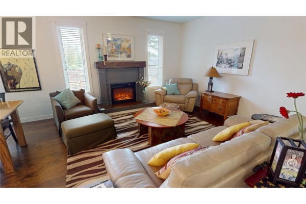 Living room with a beige sectional sofa, fireplace, wood floors, and striped rug. - 956 Copper Point Way, Invermere