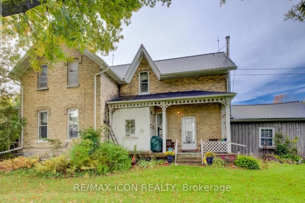 Exterior of a light-yellow brick farmhouse with a white porch and a metal roof. - 9562 Wellington Rd 16 Road, Wellington North